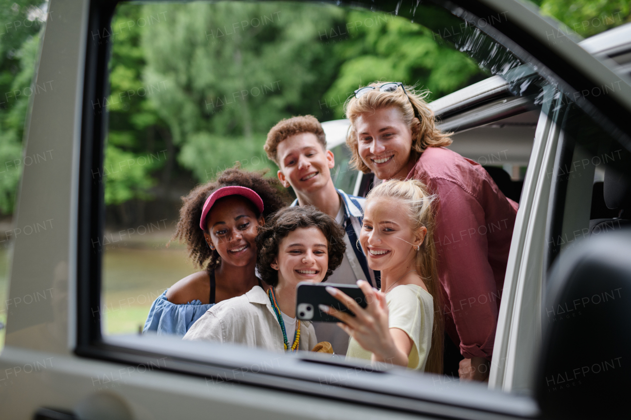 A multiracial young friends travelling together by car, taking selfie - summer vacation, holidays, travel, road trip and people concept.