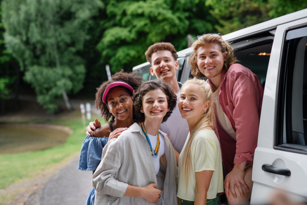 A multiracial young friends travelling together by car, looking at camera and smiling - summer vacation, holidays, travel, road trip and people concept.