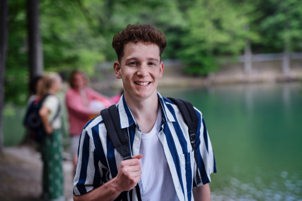 A portrait of young man with friends at background on a hiking or camping trip in the mountains in summer.