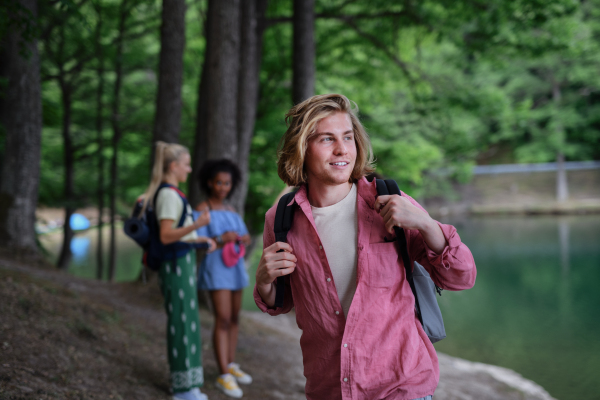 A portrait of young man with friends at background on a hiking or camping trip in the mountains in summer.