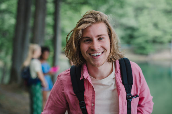 A portrait of young man with friends at background on a hiking or camping trip in the mountains in summer.