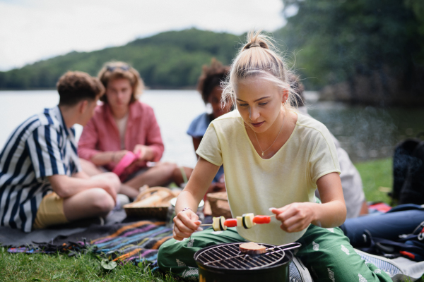 A group of multiracial young friends camping near lake and and having barbecue together.