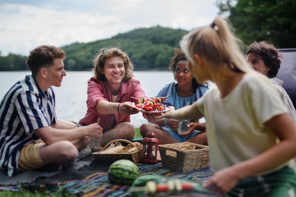 A group of multiracial young friends camping near lake and and having barbecue together, looking at camera.