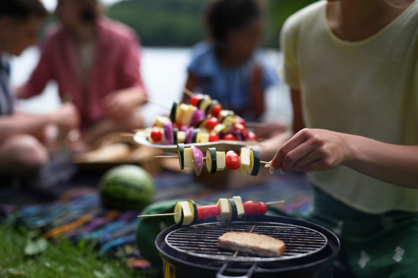 A group of multiracial young friends camping near lake and and having barbecue together. Close-up.