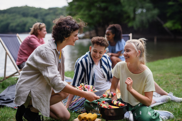 A group of multiracial young friends camping in campsite near lake and and having barbecue together.