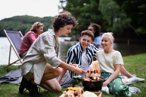 A group of multiracial young friends camping near lake and and having barbecue together.