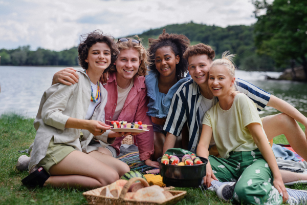 A group of multiracial young friends camping near lake and and having barbecue together, looking at camera.