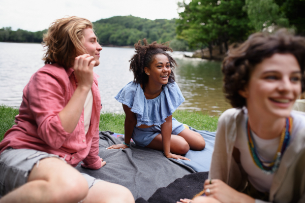 A diverse group of friends having fun together at park lauging and sitting on blanket near lake, Friendship and lifestyle concepts