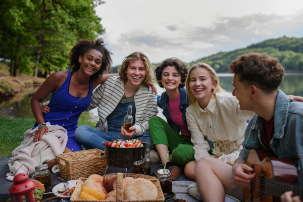 A group of multiracial young friends camping near lake and and having barbecue together, looking at camera.