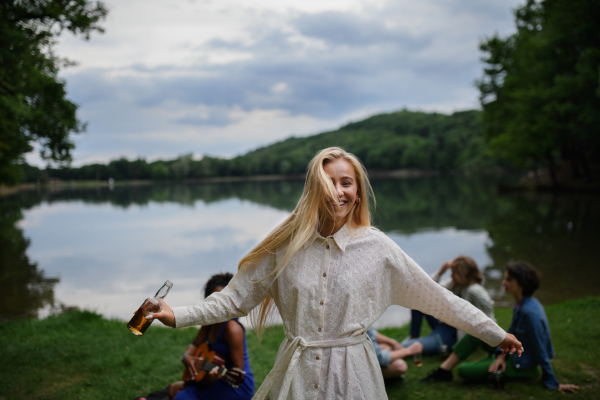 Happy young woman dancing at a camping trip with friends at the lake in summer.