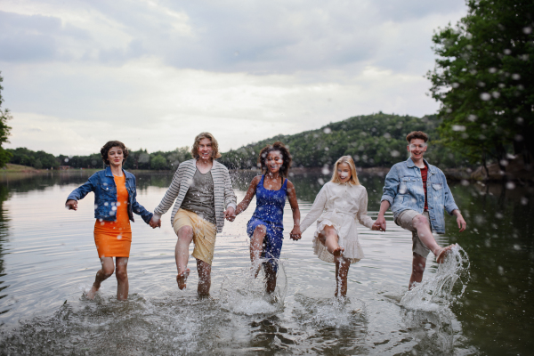 A multiracial group of young friends holding hands and standing in lake in summer.