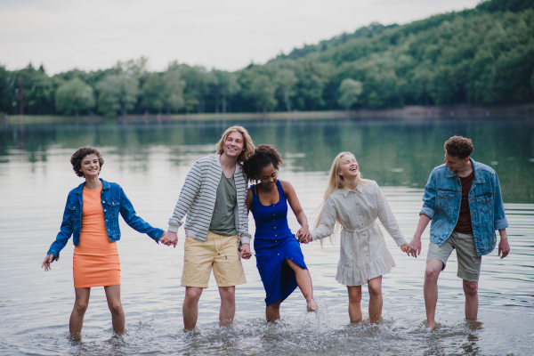 A multiracial group of young friends holding hands and standing in lake in summer.