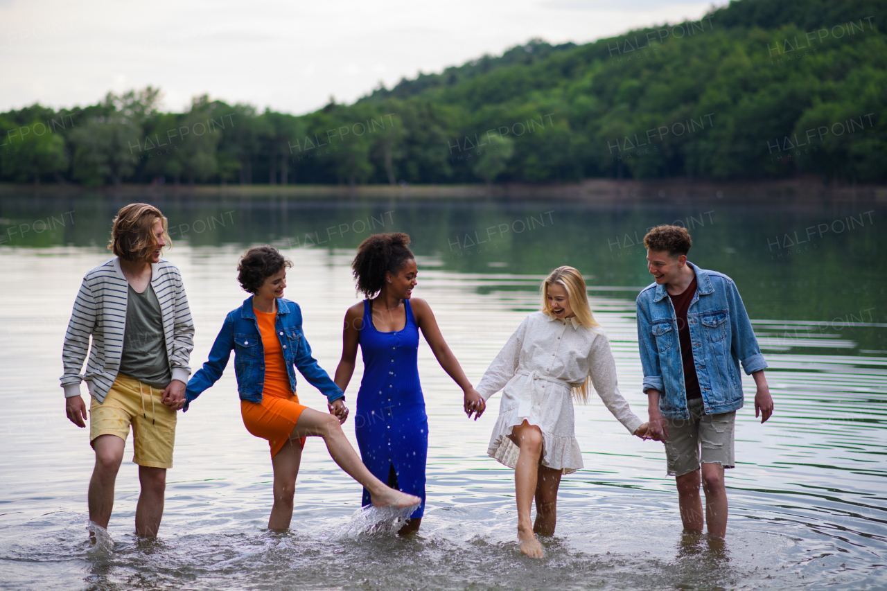 A multiracial group of young friends holding hands and standing in lake in summer.