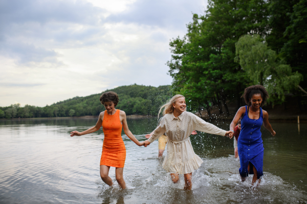 A multiracial group of young friends holding hands,standing in lake in summer and having fun.