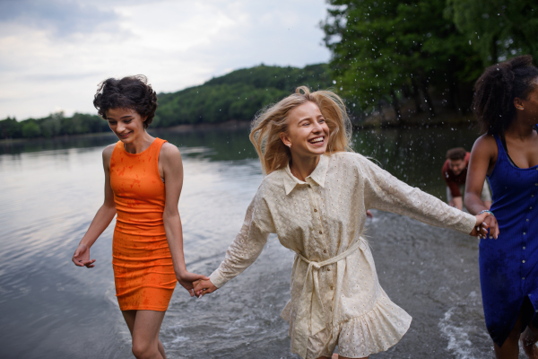 A multiracial group of young friends holding hands,standing in lake in summer and having fun.