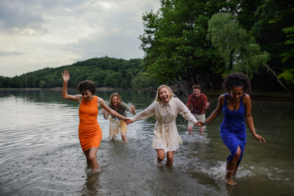 A multiracial group of young friends holding hands,standing in lake in summer and having fun.