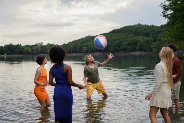 Multiracial group of young friends playing with a ball in lake during summer day and having fun