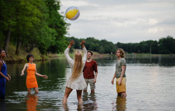 Multiracial group of young friends playing with a ball in lake during summer day and having fun