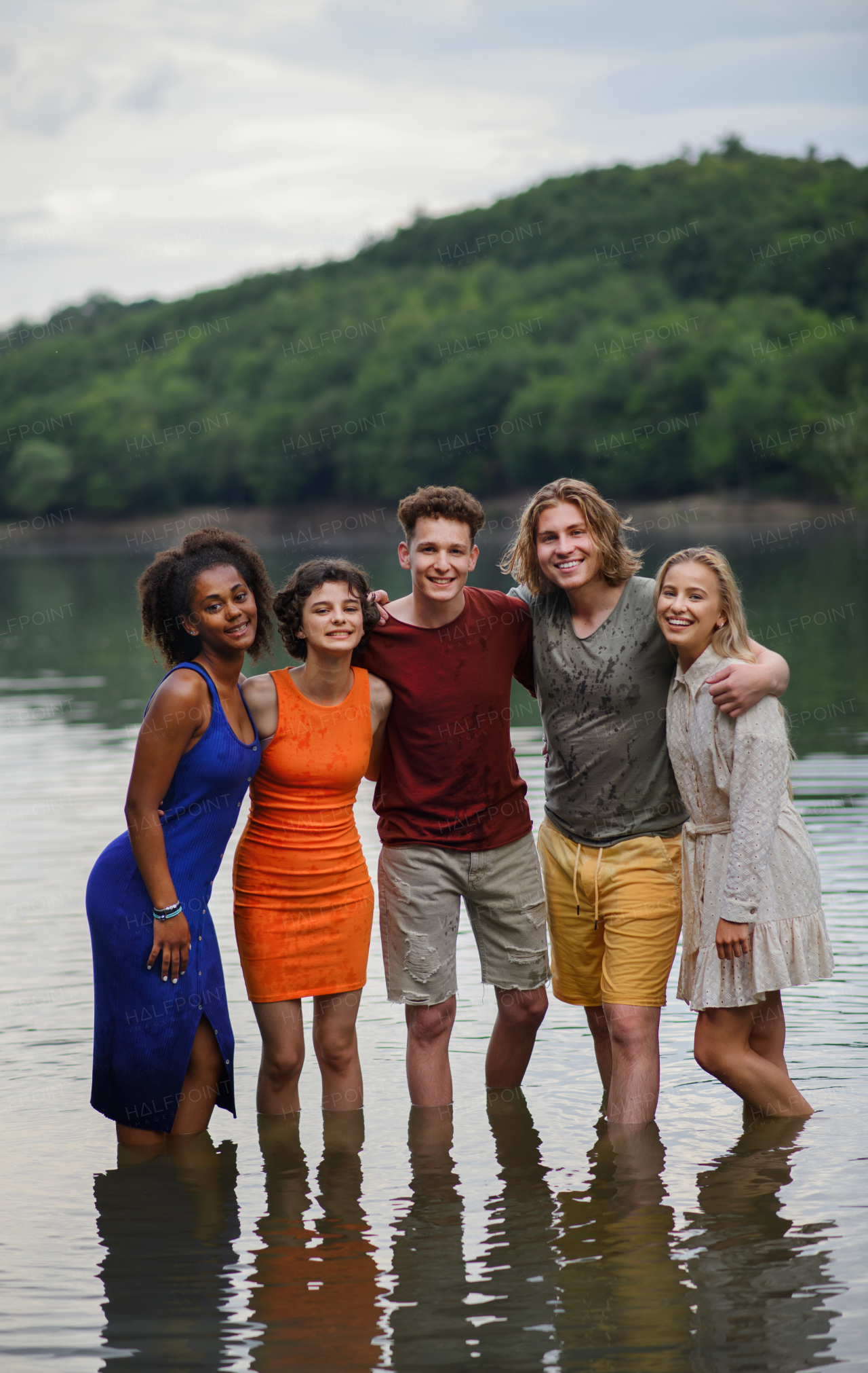 A multiracial group of young friends holding hands and standing in lake in summer.