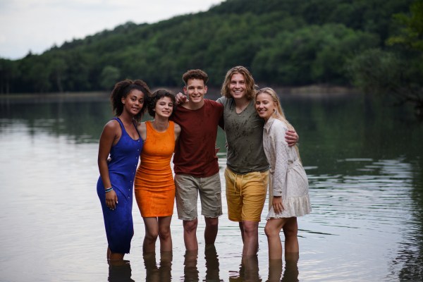 A multiracial group of young friends holding hands and standing in lake in summer.