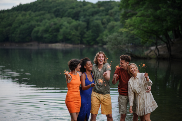 A happy group of friends lighting sparklers and enjoying freedom at beach during sunset