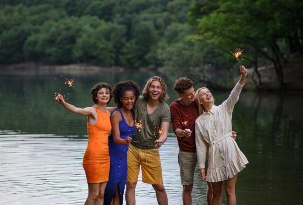 A happy group of friends lighting sparklers and enjoying freedom at beach during sunset