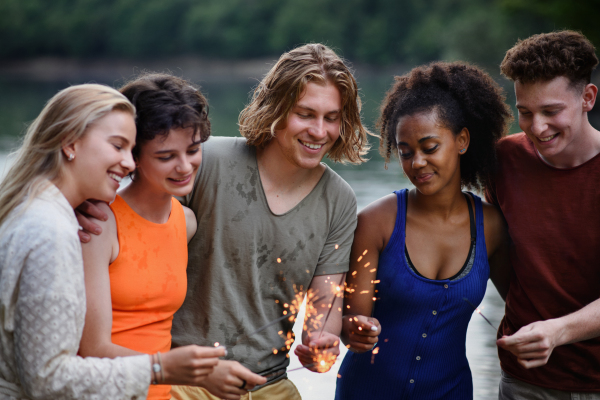 A happy group of friends lighting sparklers and enjoying freedom at beach during sunset