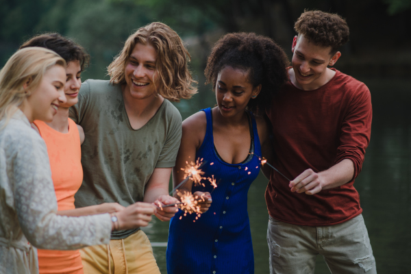 A happy group of friends lighting sparklers and enjoying freedom at beach during sunset