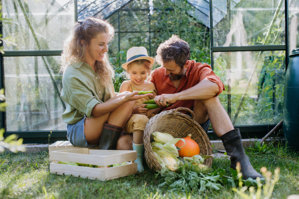 A farmer family with fresh harvest standing in front of greenhouse.