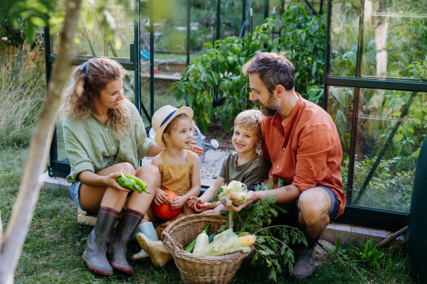 A farmer family with fresh harvest standing in front of greenhouse.