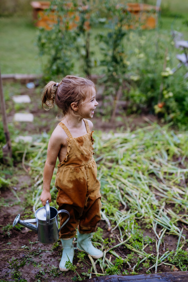 Farmer little girl having fun during watering vegetable garden together in the summer.