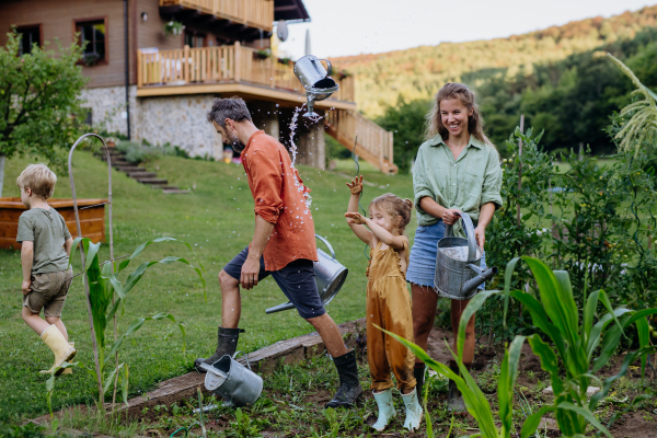 Farmer family having fun during watering vegetable garden together in the summer.