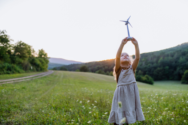 A little girl standing in nature with model of wind turbine. Concept of ecology future and renewable resources.