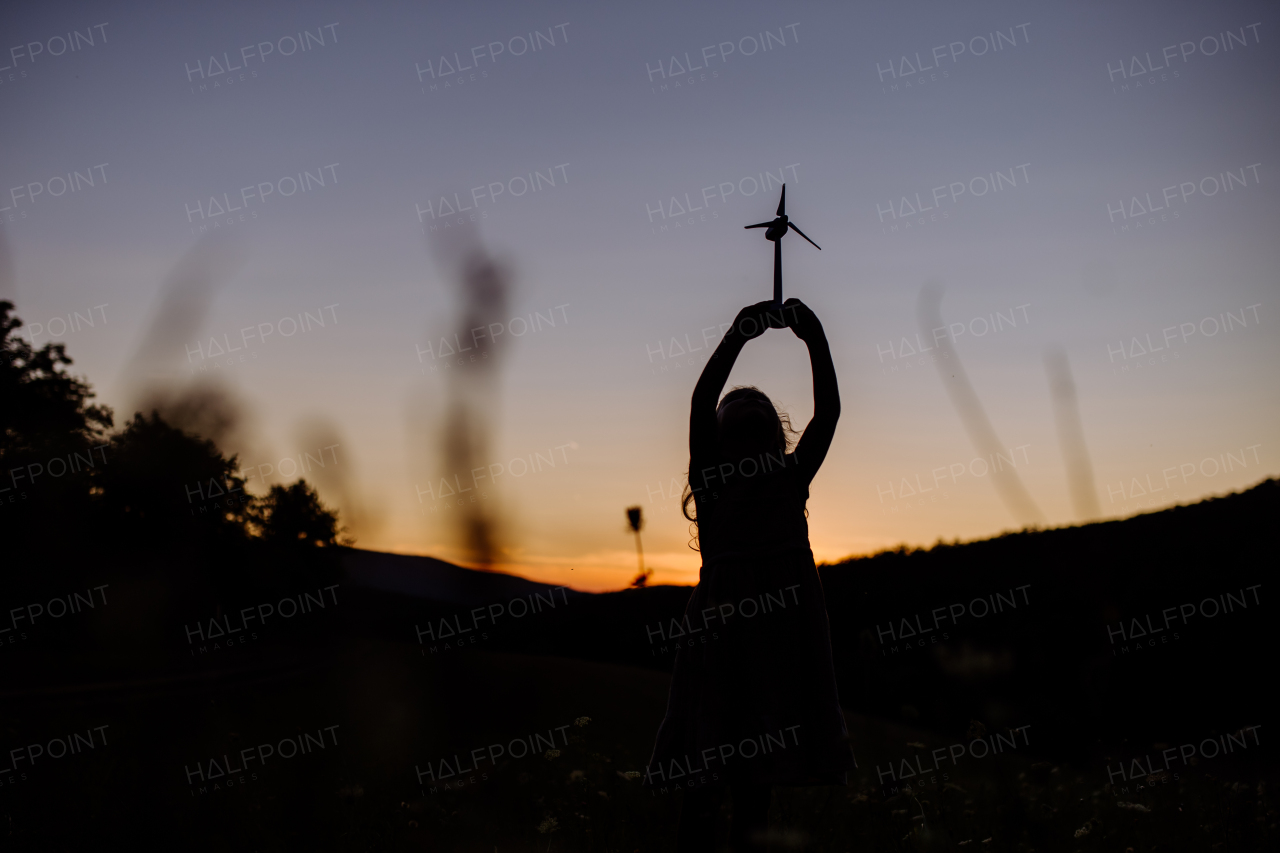 A little girl standing in nature with model of wind turbine. Concept of ecology future and renewable resources.