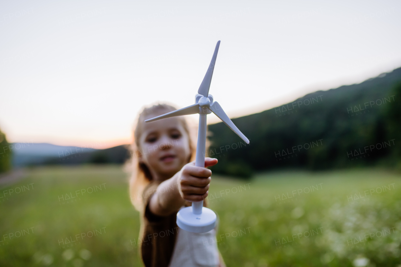 A little girl standing in nature with model of wind turbine. Concept of ecology future and renewable resources.