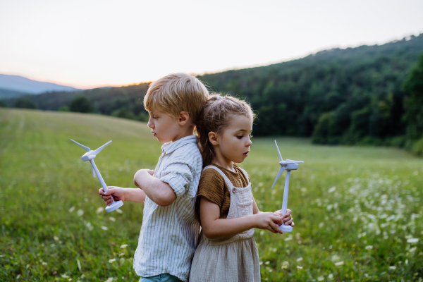 Little children standing in nature with model of wind turbine. A concept of ecology future and renewable resources.