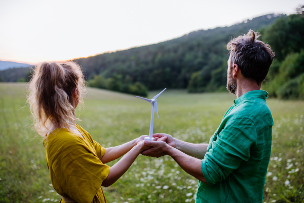 A couple standing in nature with model of wind turbine. Concept of ecology future and renewable resources.