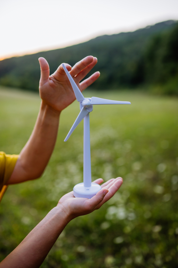 Close up of hands holding model of wind turibe in green nature. Concept of ecology future and renewable resources.