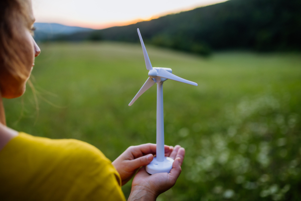 Close up of hands holding model of wind turibe in green nature. Concept of ecology future and renewable resources.