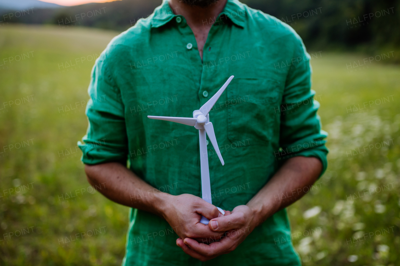 A close up of man standing in nature with model of wind turbine. Concept of ecology future and renewable resources.