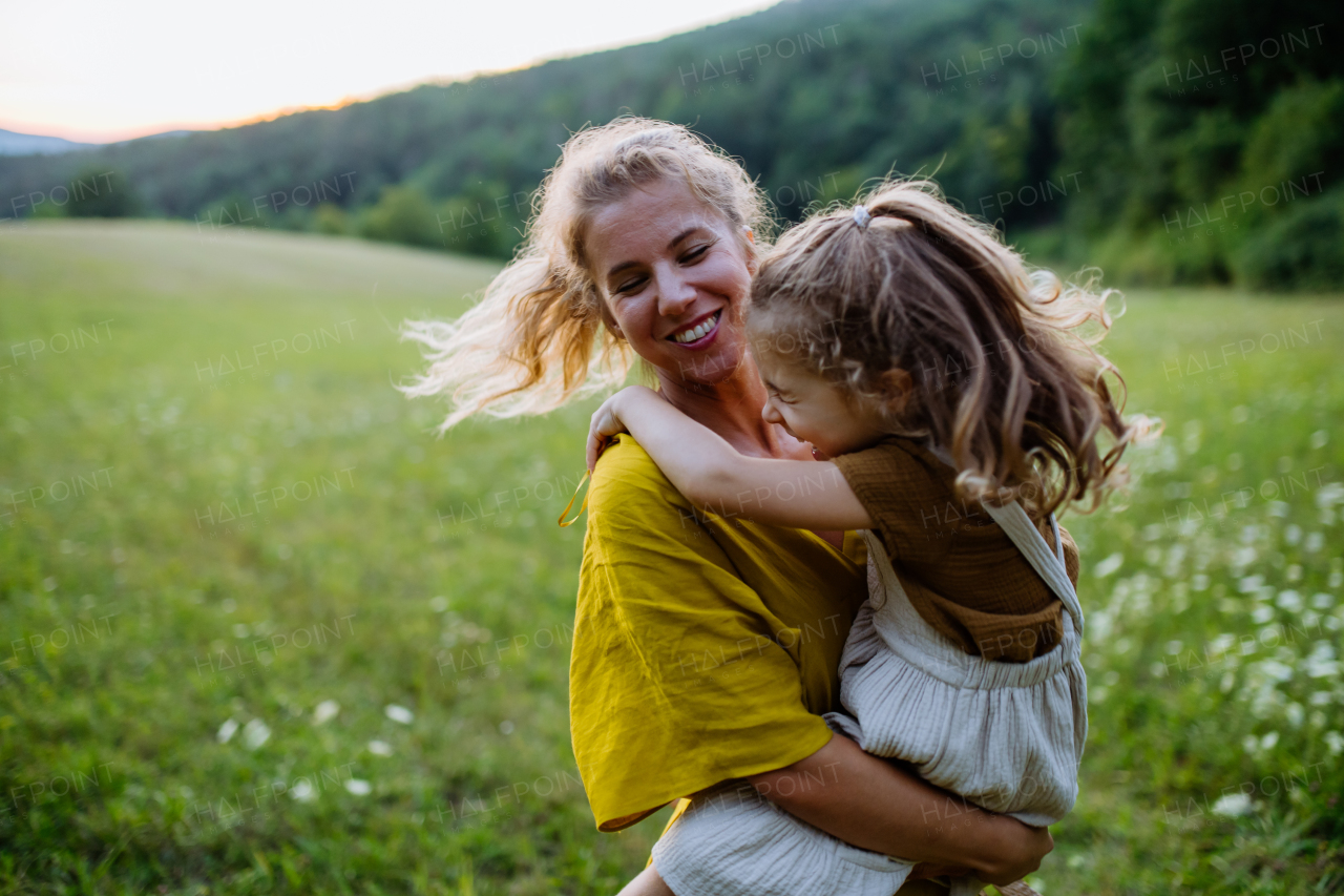 A happy mother spending time with her little daughter outside in green nature.