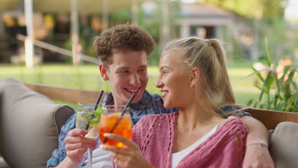 A young couple in love enjoying holiday evening together, sitting, smiling, talking and drinking coktails.