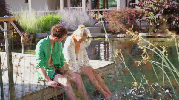 A young couple in love sitting, having legs in natural pool. Enjoying summer time.