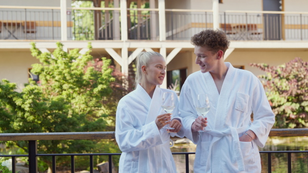 A young couple in bathrobe enjoying together time in wellness hotel, drinking wine.