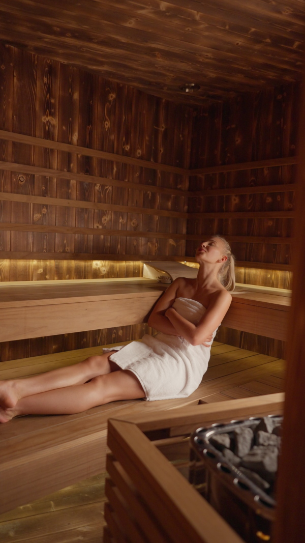 A young woman enjoying time in Finnish sauna, vertical footage.