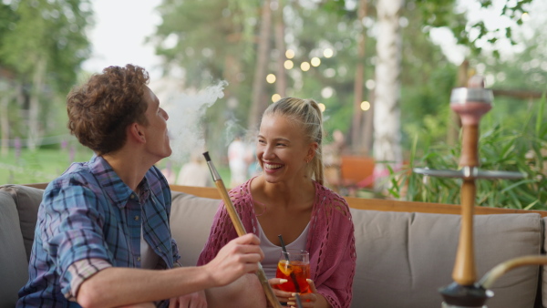 A young couple enjoying holiday time together, sitting, smiling, drinking cocktails and smoking hookach.