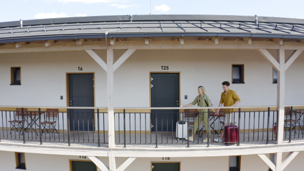 A young happy couple with suitcases arriving in hotel, walking in corridor towards rooms.