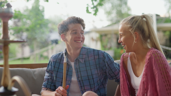 A young couple enjoying holiday time together, sitting, smiling, drinking cocktails and smoking hookach.