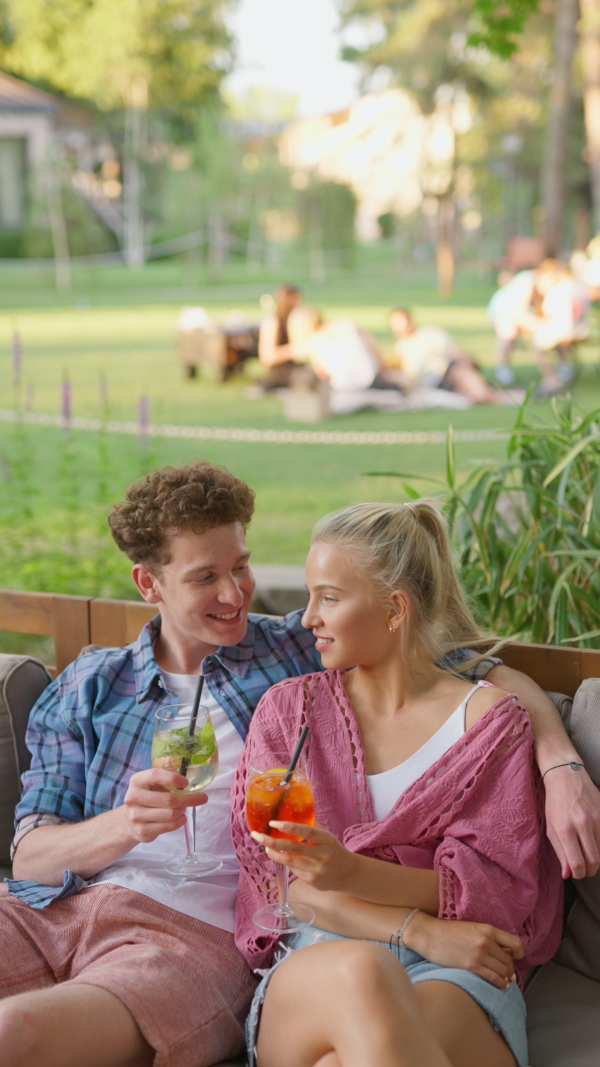 A young couple in love enjoying holiday evening together, sitting, smiling, talking and drinking coktails.