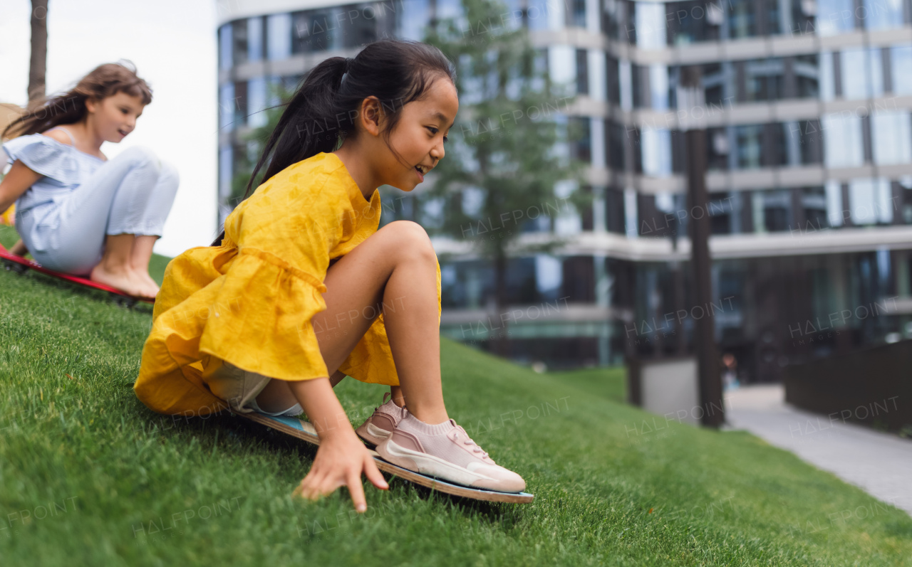 Asian girl trying to skateboarding with her friend in a city park, active kids concept.